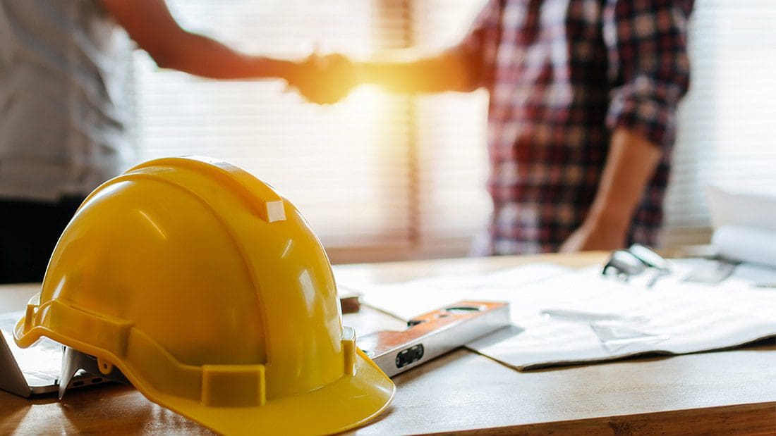 construction workers shaking hands with hard hat in foreground