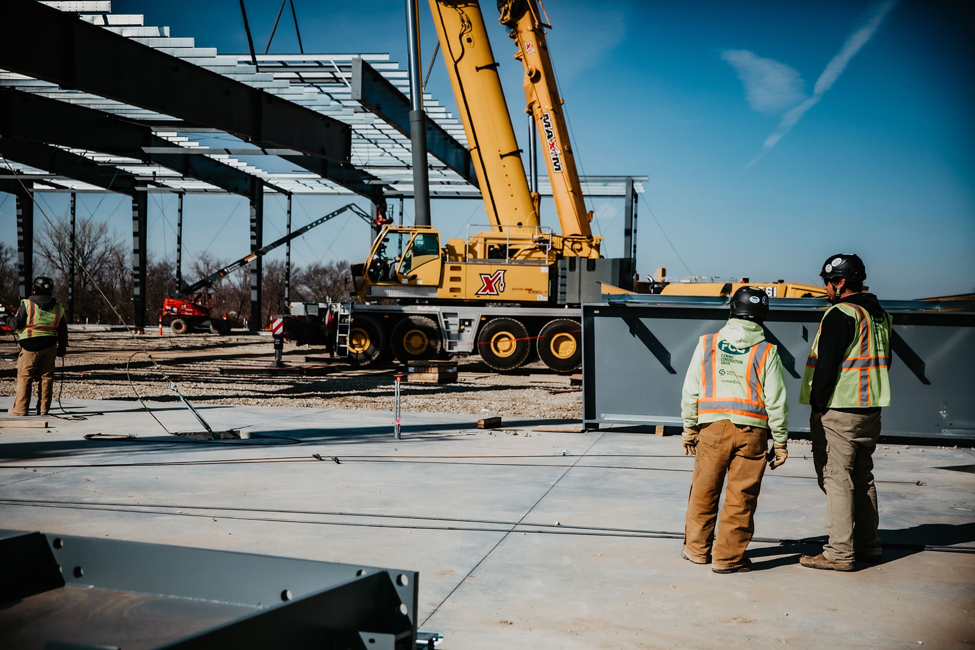 Two men on jobsite with crane wearing FCG safety vests