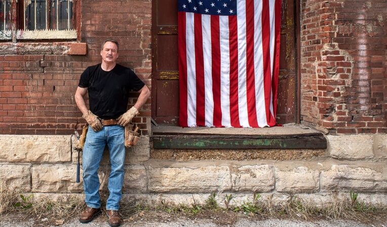 Construction worker standing in front of brick building with American flag